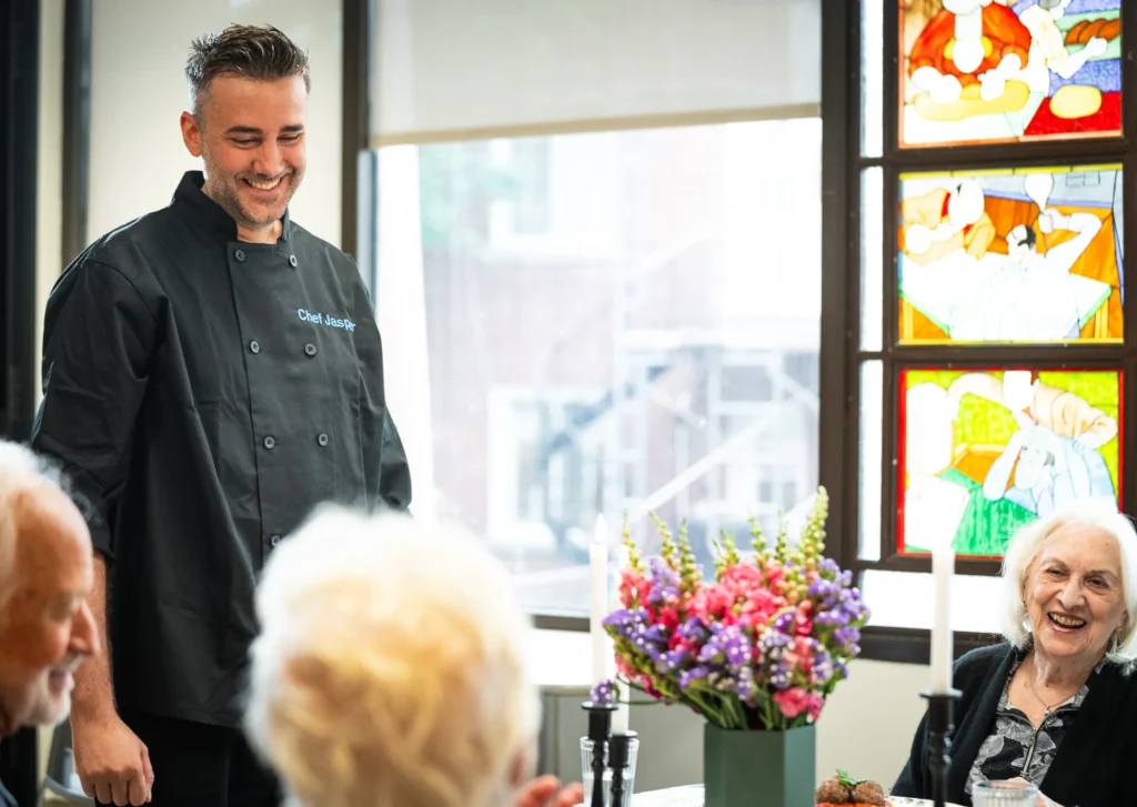 Chef Jasper chef in uniform chatting with residents at a set dining table