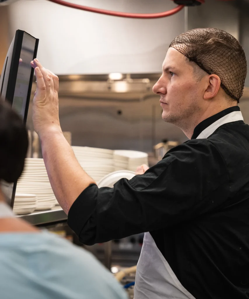Chef Jasper kitchen staff member following guidance on a workstation touchscreen